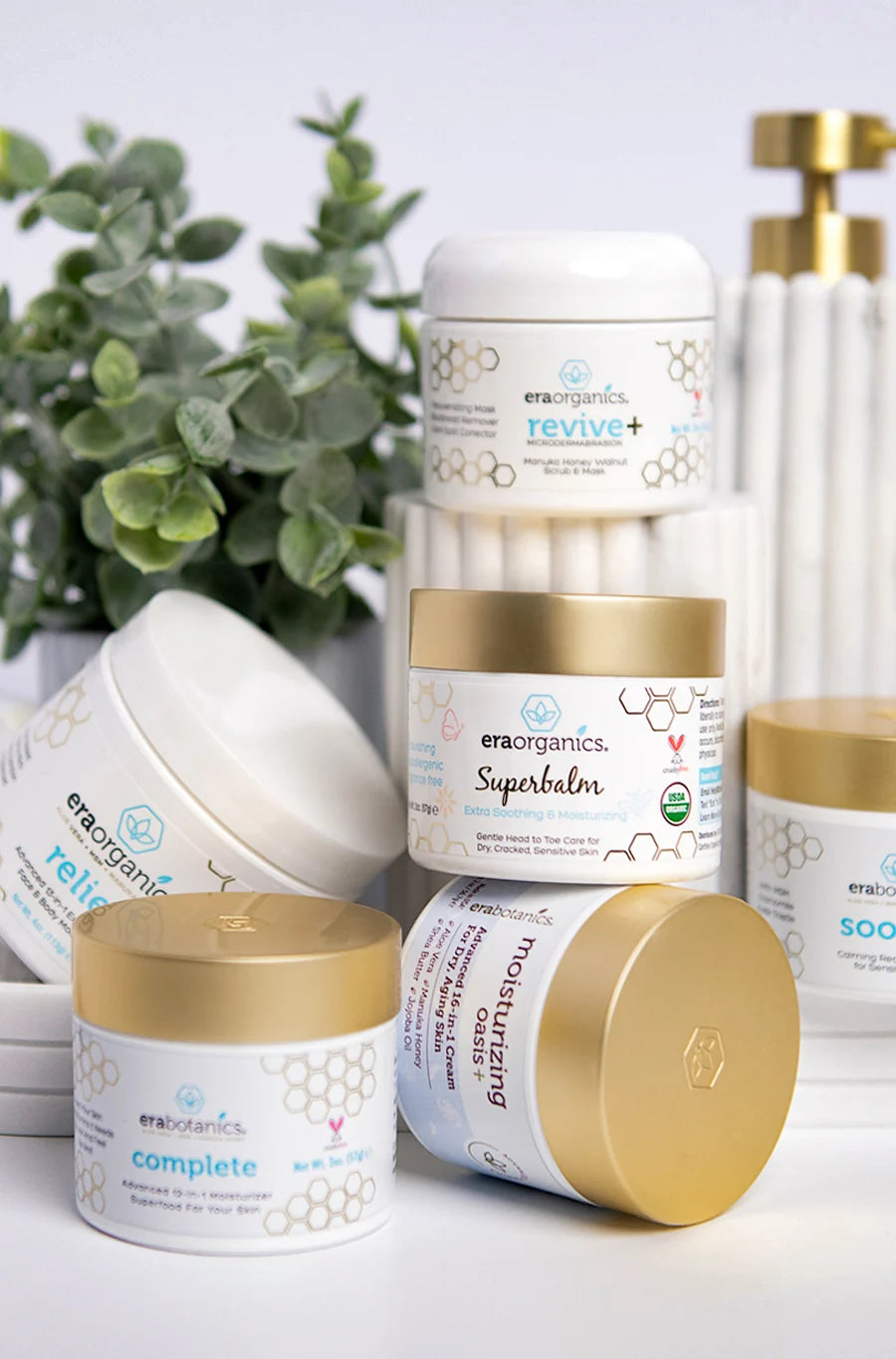 Era Organics jars, including Superbalm, Revive+ and Complete+, stacked on a bathroom vanity with a plant and a towel