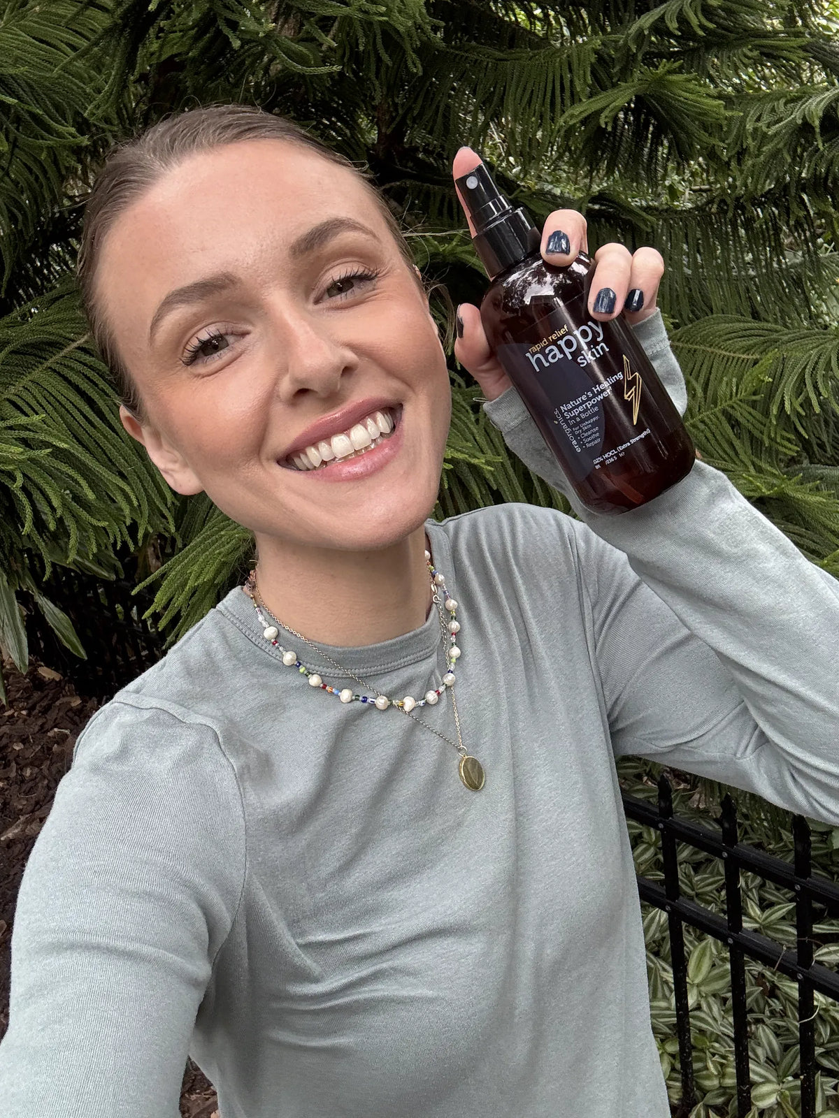Nikki Chase, Era Organics co-founder, smiling outdoors with a bottle of Happy Skin spray