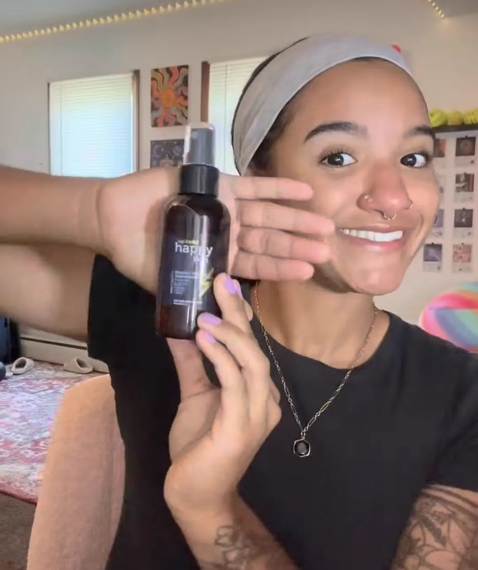 Smiling woman holding up a bottle of Happy Skin spray