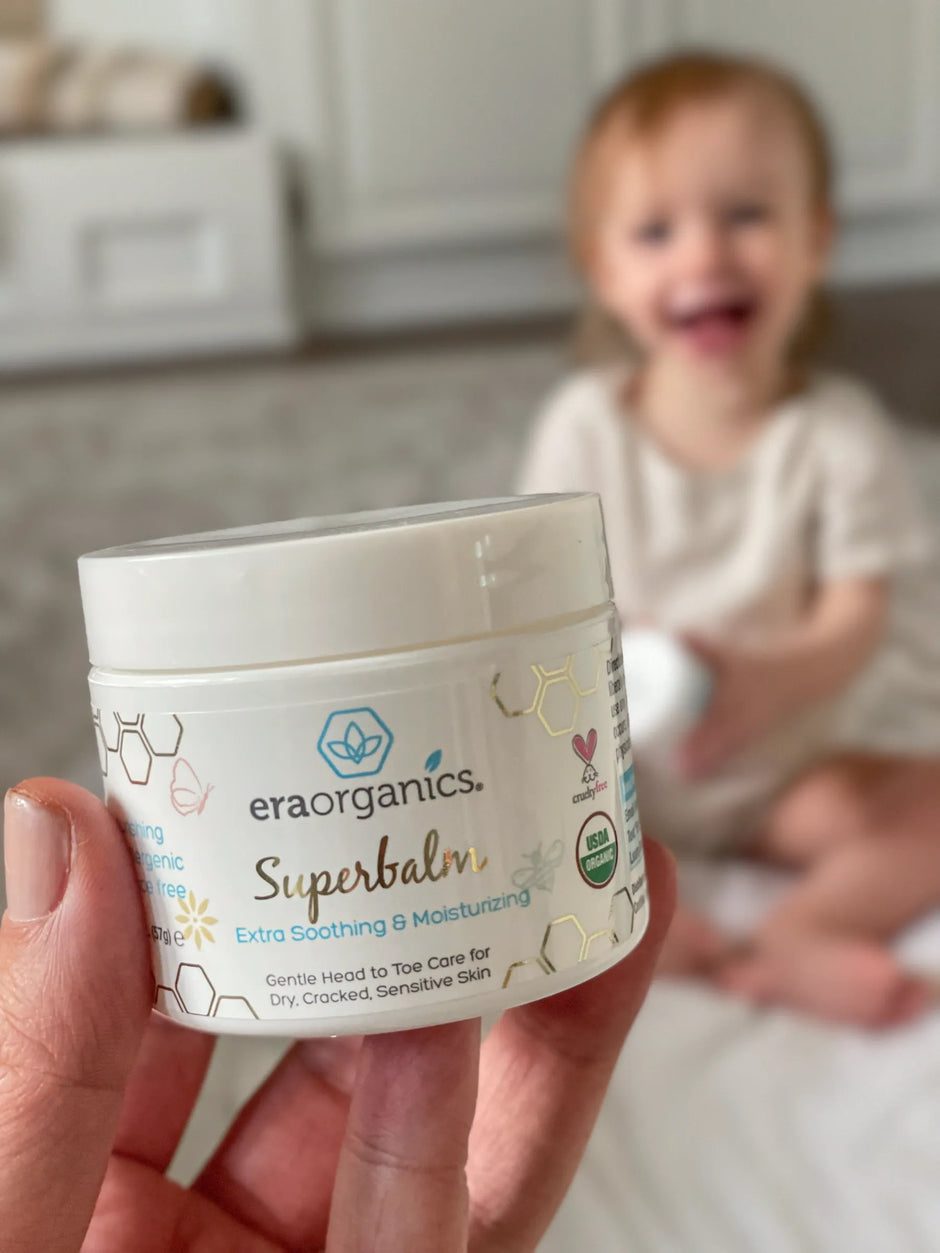 Hand holding a jar of Superbalm with a smiling toddler behind